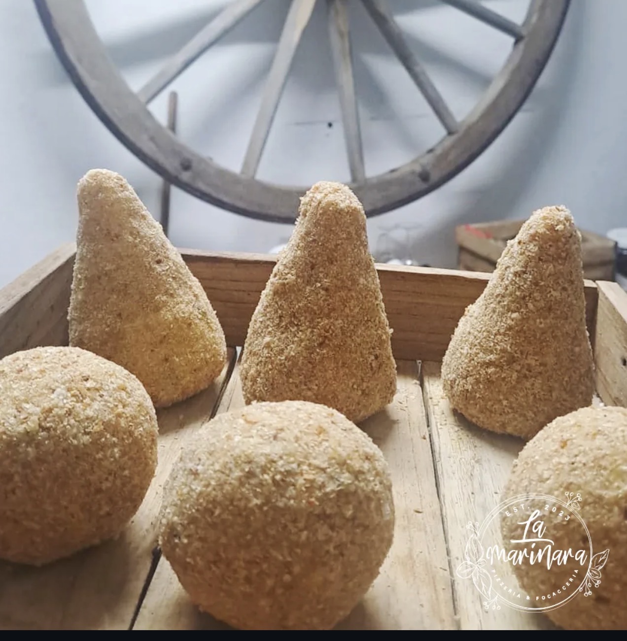 Wooden tray of hand-breaded potato croquettes and Sicilian arancini prepared at La Marinara